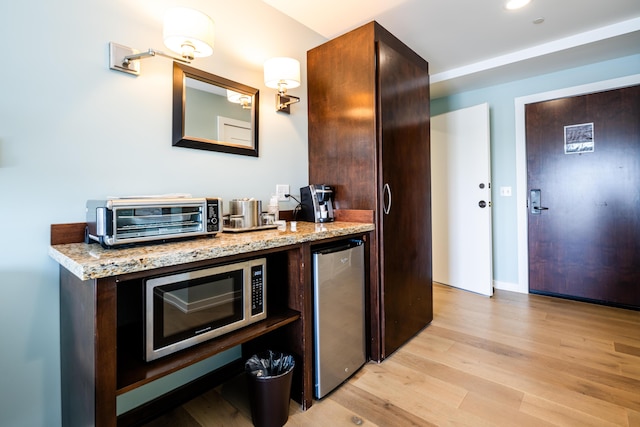 bar featuring a toaster, light wood-style flooring, stainless steel microwave, a bar, and fridge
