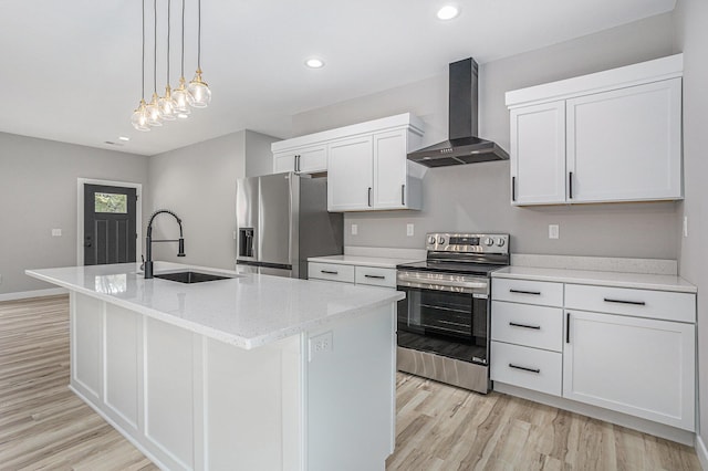 kitchen featuring light wood finished floors, stainless steel appliances, a kitchen island with sink, a sink, and wall chimney exhaust hood