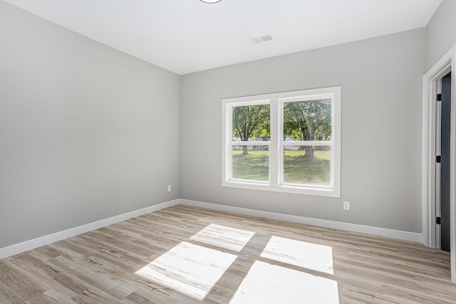 spare room with light wood-type flooring, visible vents, and baseboards