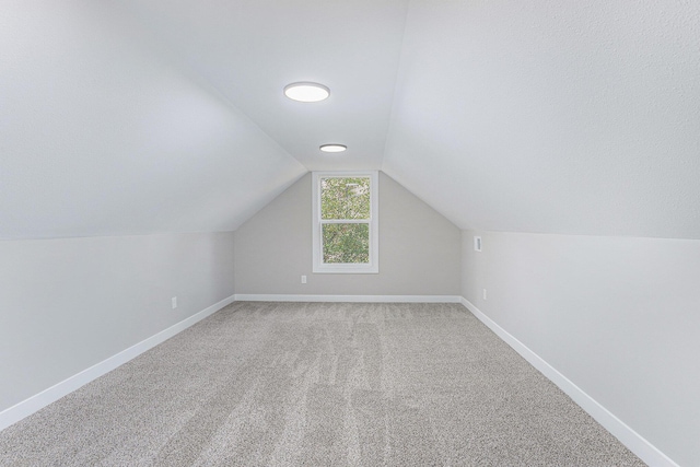 additional living space with lofted ceiling, light colored carpet, and baseboards