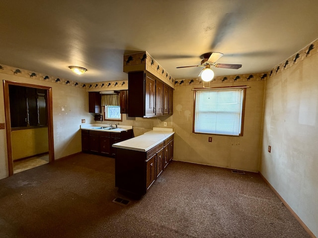 kitchen with light countertops, a sink, ceiling fan, dark brown cabinets, and a peninsula