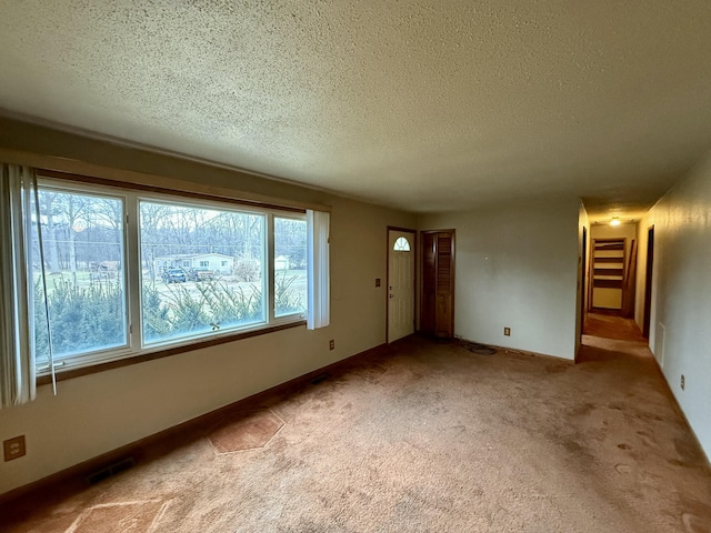 carpeted empty room featuring a textured ceiling, visible vents, and baseboards