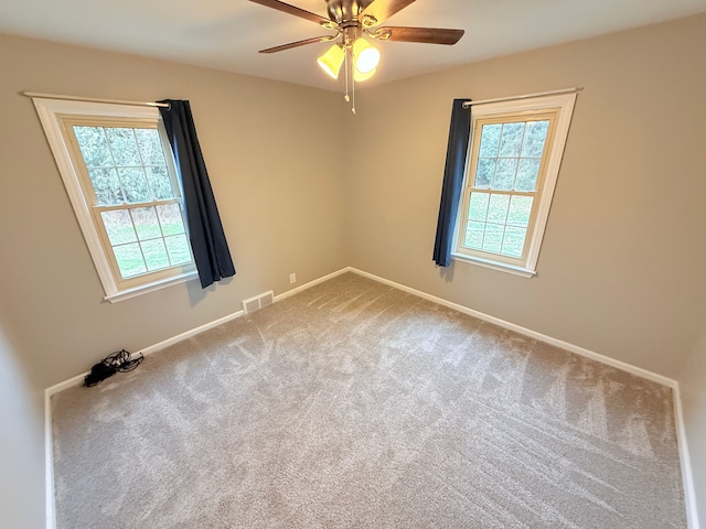 carpeted spare room with ceiling fan, a wealth of natural light, visible vents, and baseboards