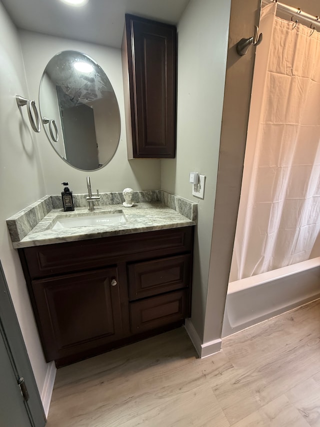 full bath with shower / tub combo with curtain, vanity, baseboards, and wood finished floors