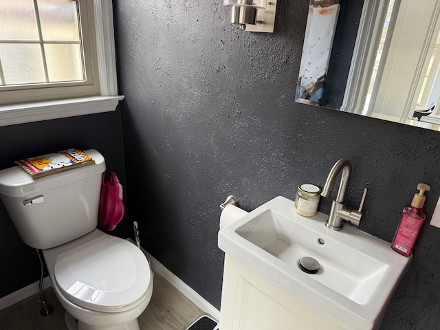 half bath with toilet, a textured wall, baseboards, and wood finished floors