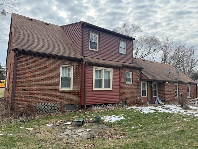 back of property with brick siding, a yard, and roof with shingles