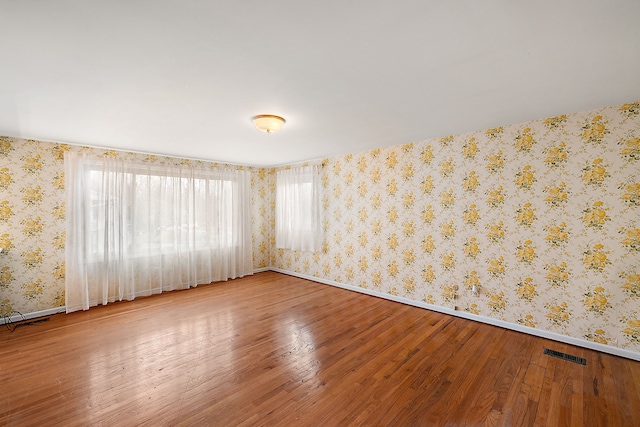 empty room featuring baseboards, hardwood / wood-style flooring, visible vents, and wallpapered walls