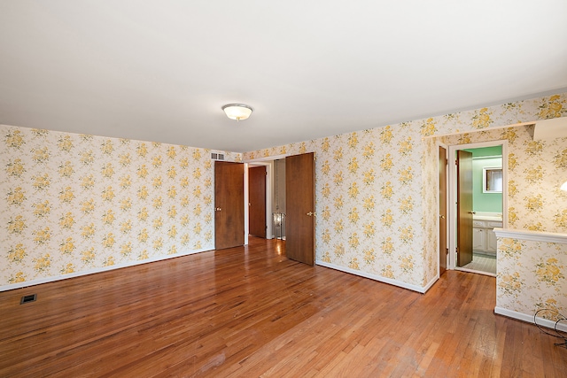 spare room featuring baseboards, hardwood / wood-style floors, visible vents, and wallpapered walls