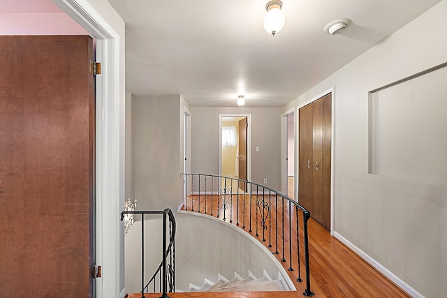 corridor featuring wood finished floors, an upstairs landing, and baseboards