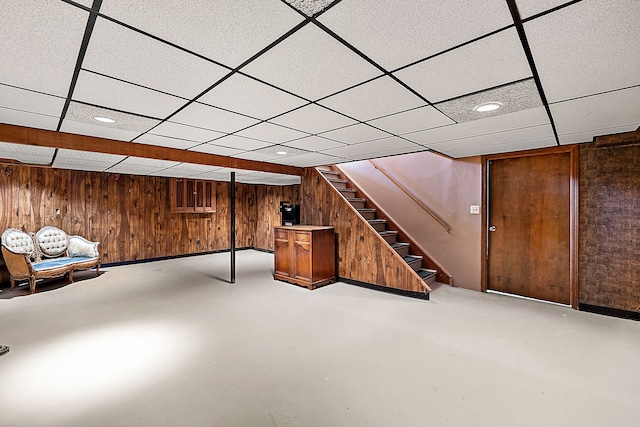 finished basement with a paneled ceiling, wooden walls, and stairway