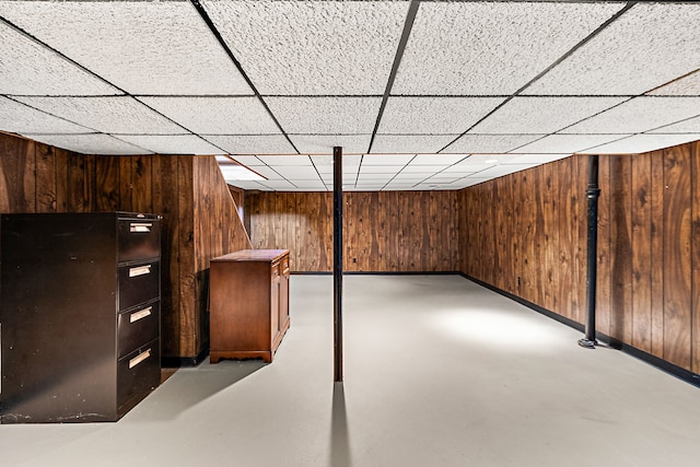 finished basement featuring a drop ceiling, wood walls, and baseboards