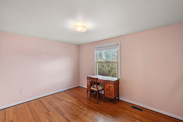 unfurnished office featuring hardwood / wood-style flooring, visible vents, and baseboards