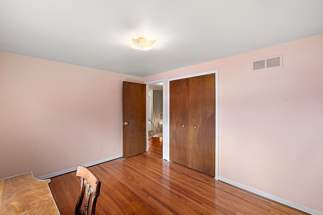 unfurnished bedroom with a closet, visible vents, baseboards, and wood finished floors