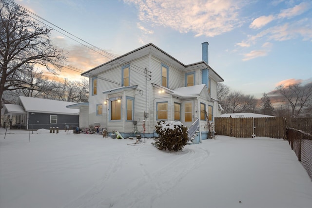 snow covered house with fence and a chimney