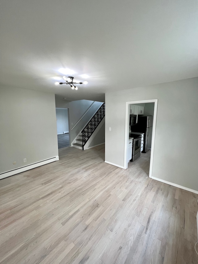 spare room featuring a baseboard heating unit, stairway, baseboards, and light wood-style floors