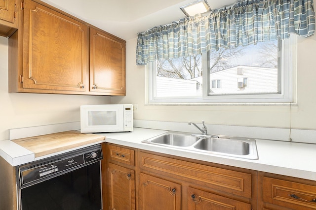 kitchen with black dishwasher, light countertops, a sink, and white microwave