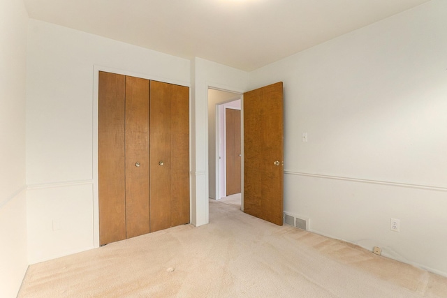 unfurnished bedroom with visible vents, a closet, and light colored carpet