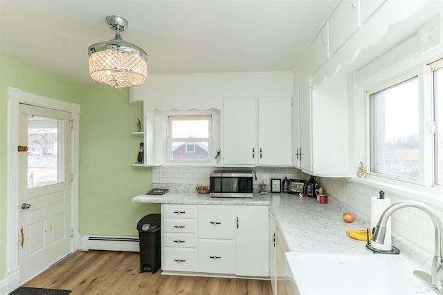 kitchen featuring a baseboard heating unit, stainless steel microwave, a sink, and white cabinetry