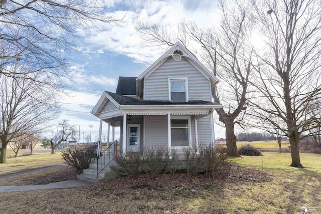 victorian-style house with a porch, a front yard, and a shingled roof