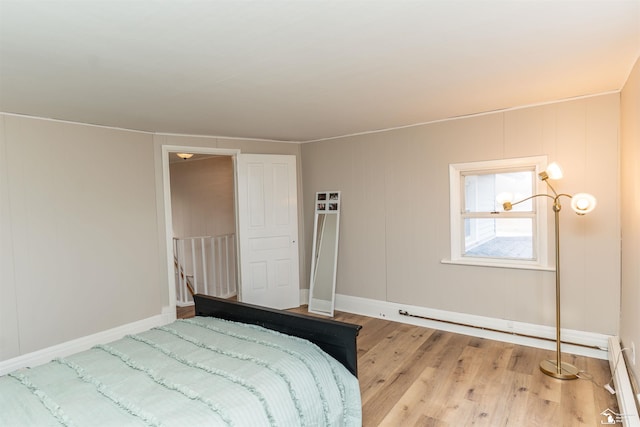 bedroom featuring a baseboard heating unit, wood finished floors, and baseboards