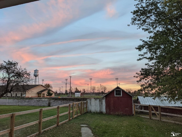 yard at dusk featuring an outdoor structure and fence