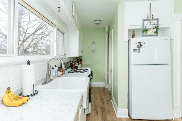 kitchen with tasteful backsplash, range with gas stovetop, freestanding refrigerator, light countertops, and white cabinetry