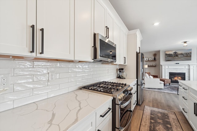 135 Barnsley Dr, Howell, MI 48843 - kitchen featuring white cabinets, a glass covered fireplace, appliances with stainless steel finishes, open floor plan, and wood finished floors