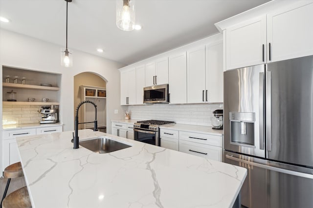 135 Barnsley Dr, Howell, MI 48843 - kitchen featuring arched walkways, an island with sink, stainless steel appliances, open shelves, and a sink