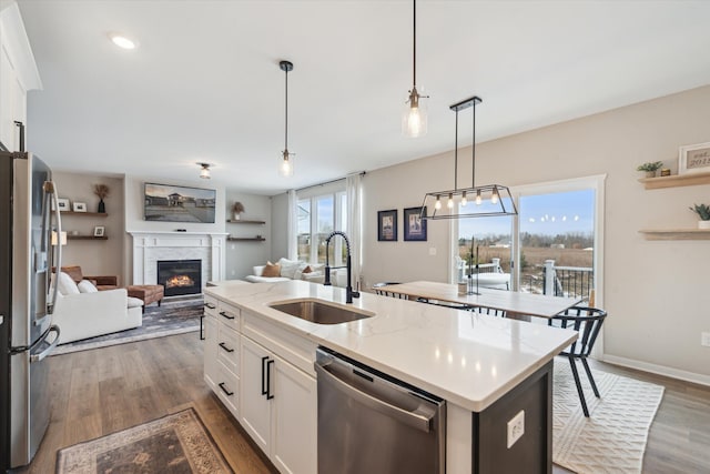 135 Barnsley Dr, Howell, MI 48843 - kitchen with stainless steel appliances, a glass covered fireplace, open floor plan, white cabinetry, and a sink