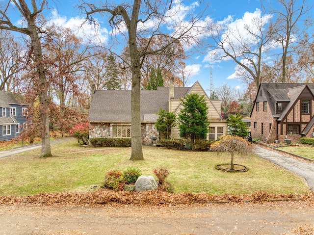 view of front of property featuring stone siding, aphalt driveway, a chimney, and a front lawn