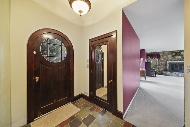 foyer with baseboards, dark carpet, and a stone fireplace