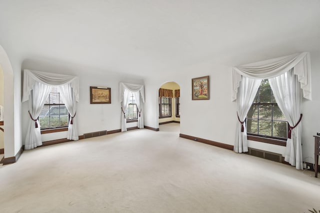 carpeted spare room featuring visible vents, arched walkways, and baseboards