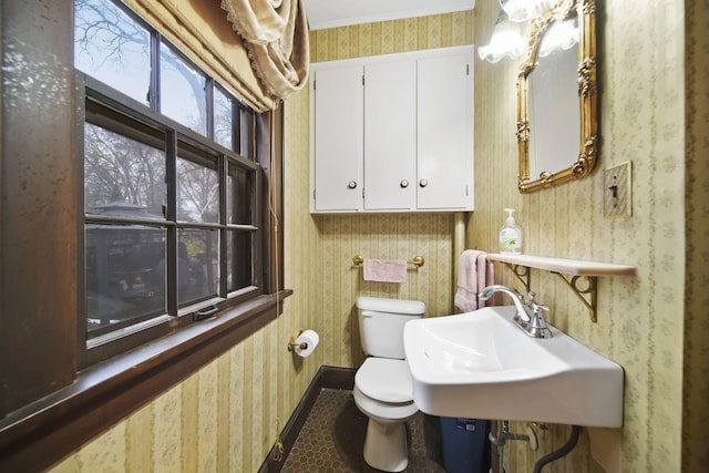 bathroom with baseboards, a sink, toilet, and wallpapered walls