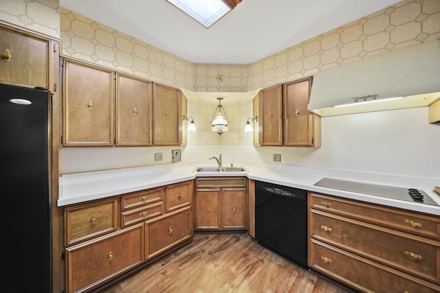 kitchen featuring wood finished floors, a sink, light countertops, brown cabinets, and black appliances