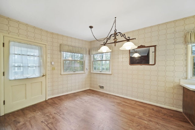 unfurnished dining area featuring visible vents, wallpapered walls, baseboards, and wood finished floors