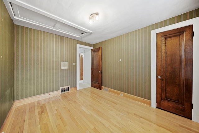 unfurnished room featuring attic access, visible vents, wallpapered walls, and wood finished floors