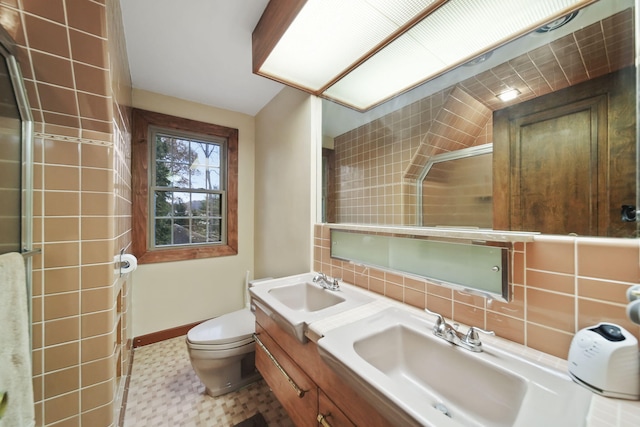 bathroom featuring toilet, a shower with shower door, a sink, and baseboards