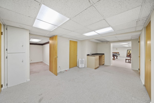 finished basement with a paneled ceiling, baseboards, and light colored carpet