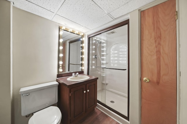 bathroom with a paneled ceiling, toilet, wood finished floors, vanity, and a stall shower