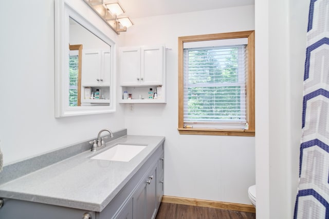 bathroom with toilet, wood finished floors, vanity, and baseboards