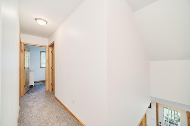 hallway with lofted ceiling, light colored carpet, and baseboards