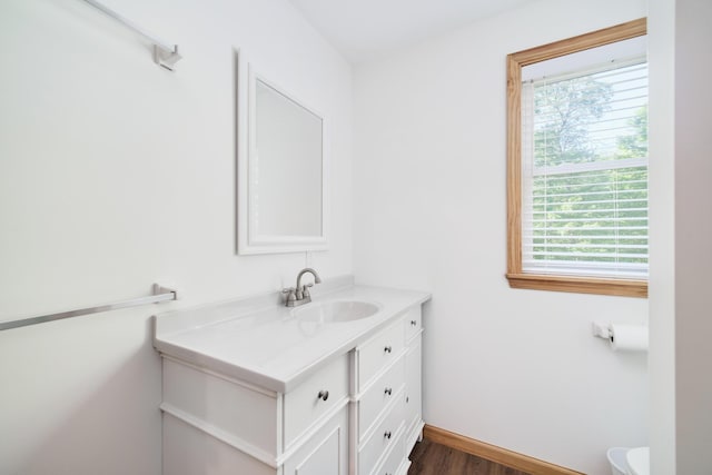 half bath with baseboards, vanity, toilet, and wood finished floors