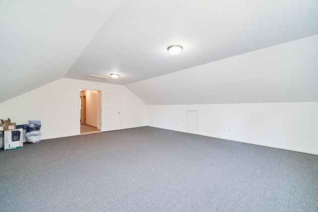 additional living space featuring dark colored carpet, vaulted ceiling, and baseboards