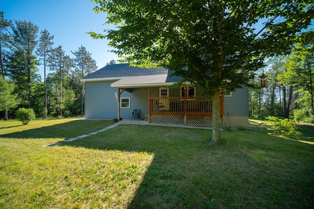 rear view of house featuring roof with shingles, a lawn, and a wooden deck