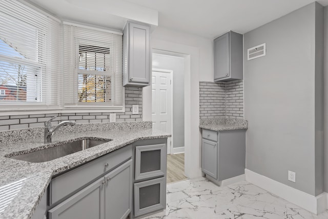 kitchen with marble finish floor, baseboards, a sink, and gray cabinetry