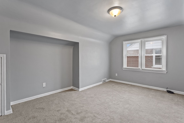 empty room featuring lofted ceiling, carpet, visible vents, and baseboards