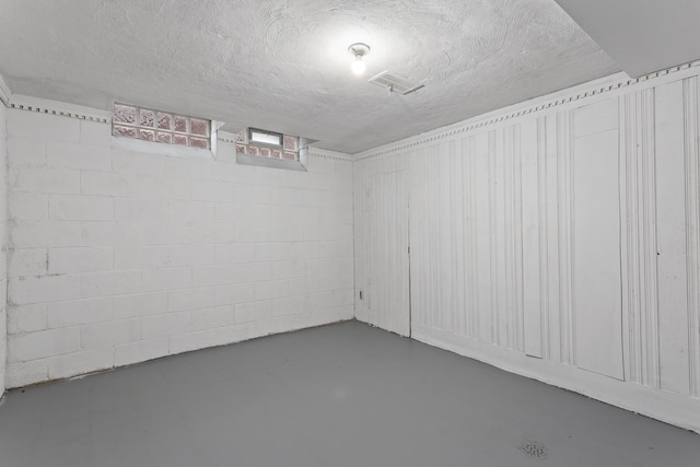 finished basement with concrete block wall, visible vents, and a textured ceiling