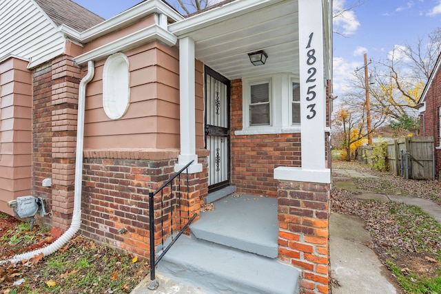 entrance to property with a shingled roof, brick siding, and fence