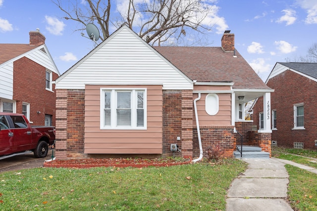 bungalow-style home featuring a shingled roof, a front yard, brick siding, and a chimney