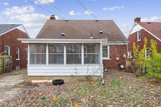 rear view of house with brick siding, a chimney, a shingled roof, a sunroom, and fence